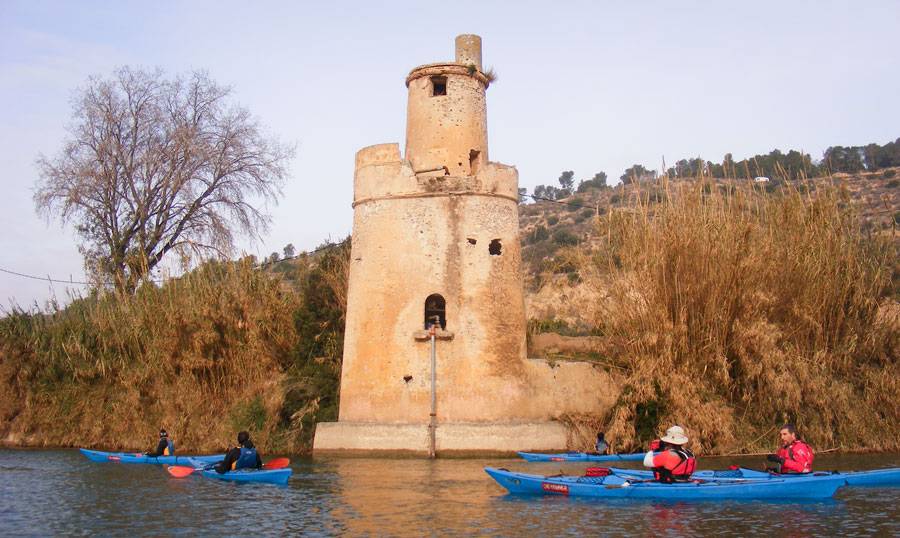 gent anant en piragua per l'Ebre, passant per davant de la torre de Mollet, al terme de Benifallet 